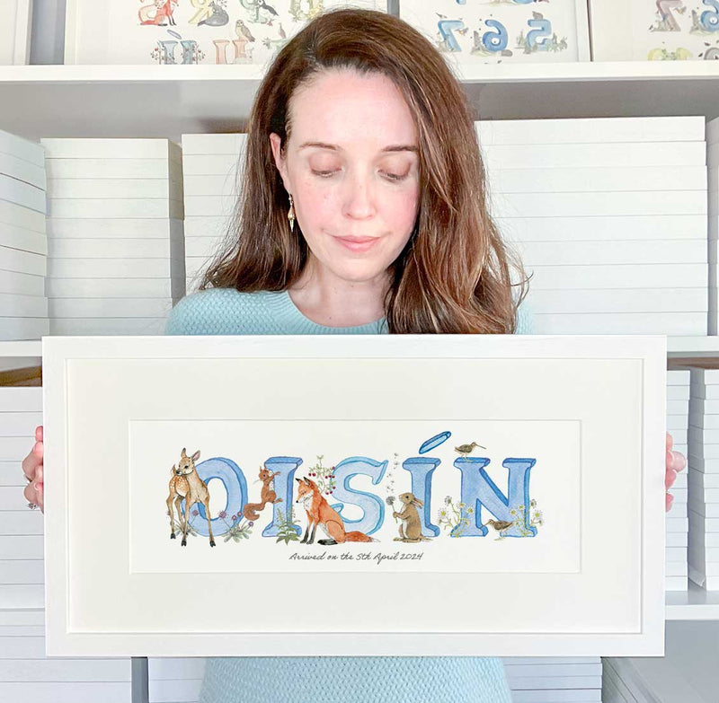 Tanya from Fiadh and Finn holding a personalised alphabet baby name frame in blue watercolour print of the Irish name Oisín.