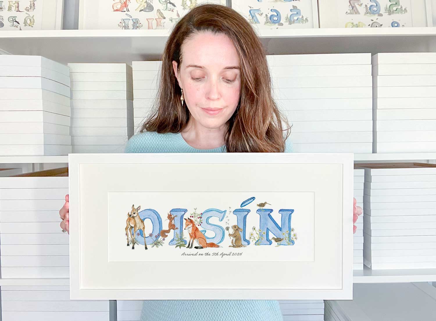 Tanya from Fiadh and Finn holding a personalised alphabet baby name frame in blue watercolour print of the Irish name Oisín.