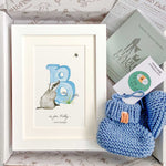 Baby gift box with blue watercolour alphabet letter in white frame and blue knitted baby booties. Booklet included